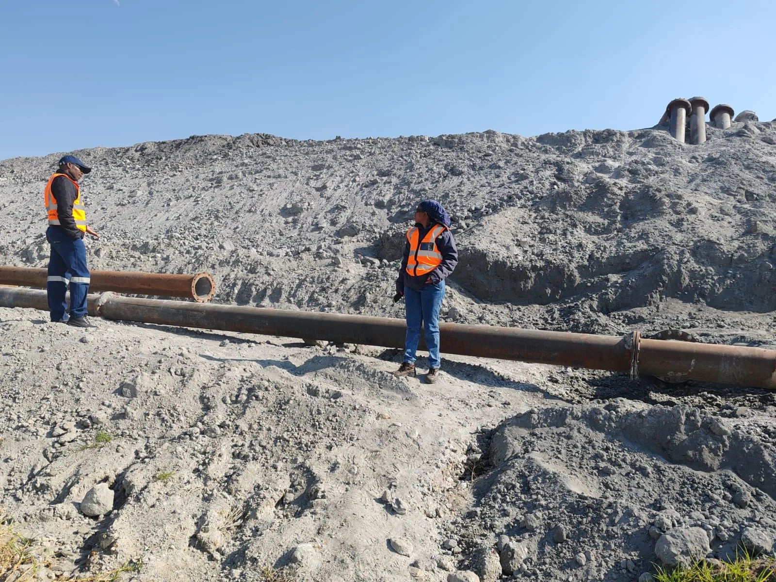 Feasibility studies site assessment – engineers in safety vests inspecting pipes and ground conditions for a development project.