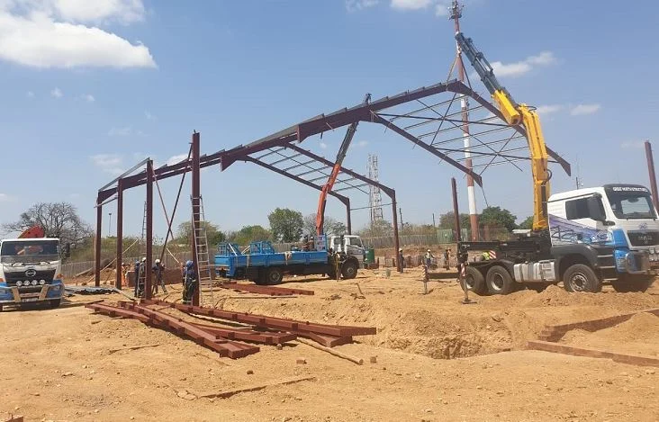 Project management team overseeing steel structure construction with cranes and trucks on site